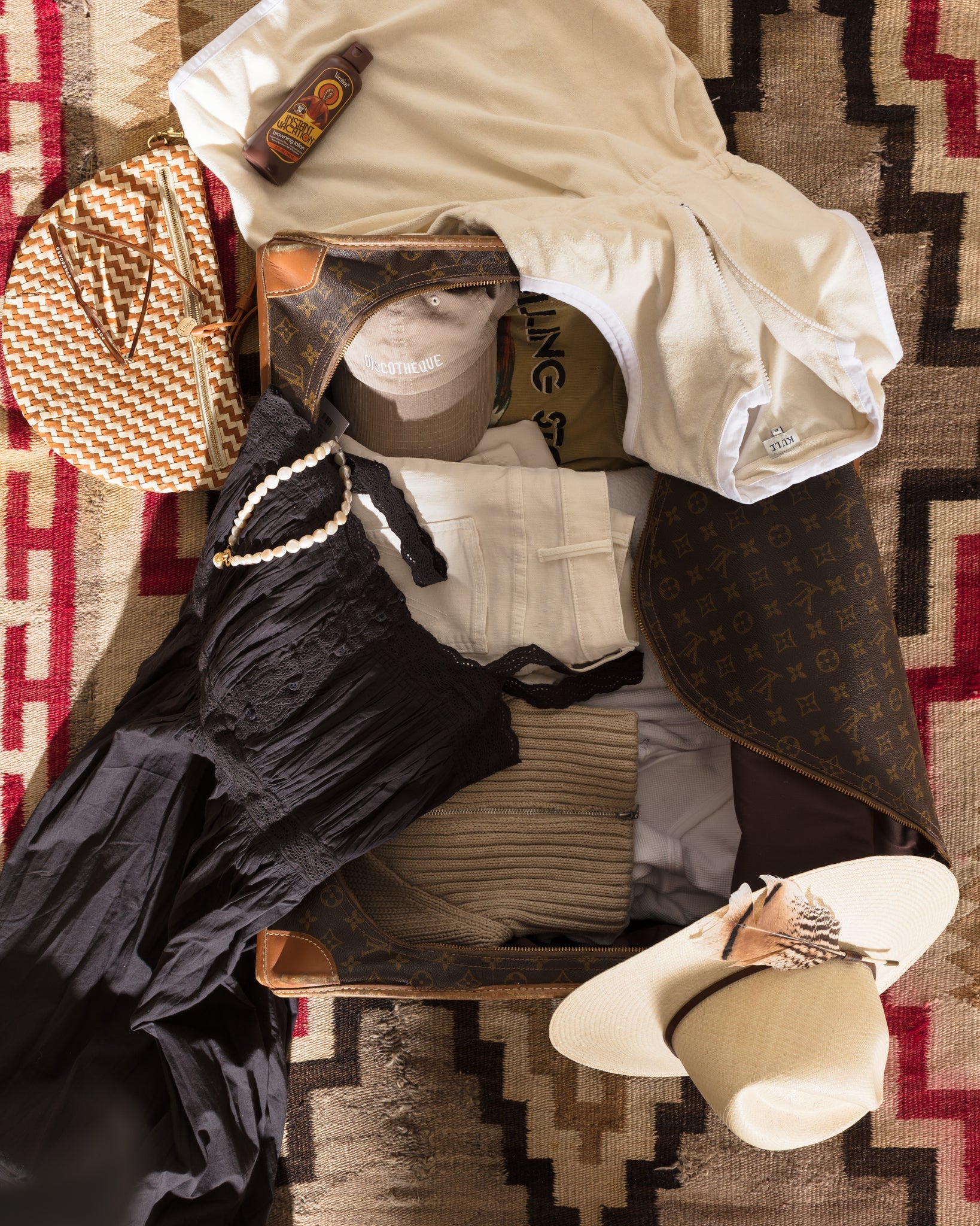 A suitcase with clothes and hats on a rug.