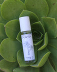 A 10ml bottle of MAYA NO.1 by Maya Fragrances, featuring a white cap and a palm tree label, rests on green succulent leaves, capturing the essence of an exotic escape.