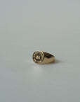 The Faire "Everything Will Be OK Ring" is a gold-plated signet, engraved with "ALL THINGS EVENTUALLY" in a circular pattern around a small central symbol, shown resting on a light gray surface.