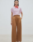 A woman stands against a plain background wearing SUNCOO’s Woven Pantalon Jayden, a pink striped top, white studded shoes, and a red scarf tied at her neck. Her hands are in the pockets of the wide-leg pants with a drawstring waistband.