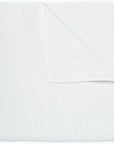 A plain white textured blanket neatly folded over in a Scottsdale Arizona bungalow, displaying a smooth and soft quilted pattern.
