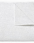 A white fabric with a black dashed line pattern, neatly folded. The texture appears soft and lightweight, ideal for bedding or clothing material in a Scottsdale Arizona bungalow featuring the John Robshaw Coverlet King.