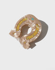 The Fashion Hair Clip by Faire is a beige, pearlescent horseshoe-shaped accessory made from eco-friendly cellulose acetate, featuring yellow glitter accents, blue rhinestones, and star details, displayed on a white surface.