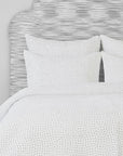A neatly made bed in a Scottsdale, Arizona bungalow, featuring a white patterned duvet cover and matching pillows set against a headboard with a black and white streaked design by John Robshaw.