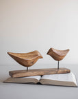 The Faire Arlo Natural Wood Decorative Birds feature two hand-carved mango wood birds on metal rods and a wooden base. Their simple design makes them an ideal accent for boho decor.