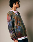 A person with short dreadlocks stands sideways against a neutral background, wearing the Riverside Tool & Dye Cashmere V-neck over a pink shirt.