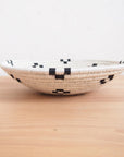 The Maraba Small Bowl by Amsha - Faire is a shallow, round sisal basket featuring a white base with black geometric patterns—ideal as wall art or a unique accent piece.