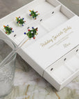 The Tree Glass Swizzle Sticks S/4 by Be Home, featuring glass tree-shaped tops with colorful dots, is displayed beside a clear glass with a frosted leaf pattern on a marble surface.