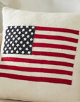 The American Flag Wool Pillow by Faire, made from hand-felted wool with blue, white, and red stitched details, sits on a beige armchair—a perfect handmade décor accent for any cozy space.