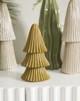 The Village Tree Small by Accent Decor, a gold ceramic tree figurine, is showcased on a white surface among white and green tree sculptures, forming a festive holiday display inspired by the Village Collection.