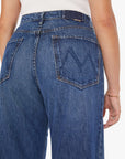 A person wears Mother’s The Half-Pipe Ankle jeans—super high-waisted, wide-leg denim in dark blue with a stitched "M" on the back pocket—and a white top; their right arm shows a delicate bracelet.
