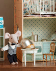 Two Maileg toy mice dressed as waiters stand in a vintage kitchen and dining room. One lifts the Maileg Cheese Bell, revealing a tasty treat, while a milk carton sits on top of the refrigerator nearby.