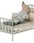 A Maileg Mouse in pajamas rests on its back in a Maileg Furniture metal bed with patterned bedding and a pillow, perfect for dollhouse setups.
