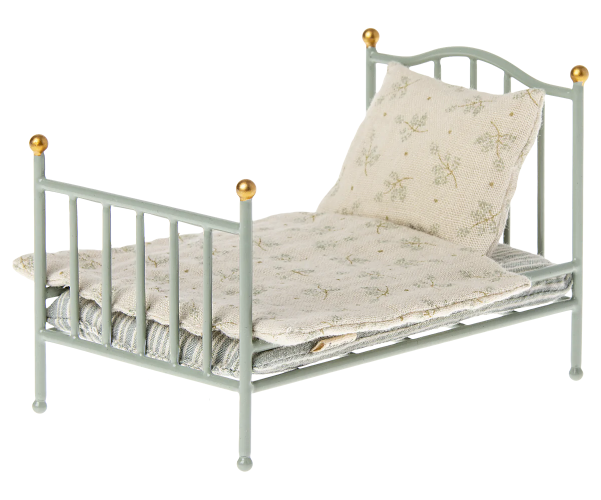 The Maileg Furniture bed by Maileg is a small, light blue metal dollhouse piece with gold-tipped posts, including a white pillow and floral blanket—a delightful addition to any collection.