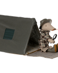 A Maileg toy mouse sits at the entrance of the Maileg Happy Camper Single Tent, dressed in plaid clothes and a hat, holding a magnifying glass. The cozy gray tent features a square window and front mat for imaginative play.