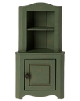 The Maileg Furniture by Maileg is a small green wooden corner cabinet for dollhouses, featuring an upper open shelf with two sections and a lower cupboard door with a round handle, shown against a plain white background.