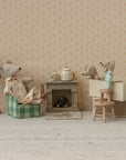 Three toy mice relax in a Maileg home, complete with the Maileg Fireplace, green chair, blue stool, teapot, lamp, and tiny furniture set against floral wallpaper for a charming vintage look.