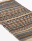 A close-up of the Maileg Rug by Maileg shows its woven texture with horizontal stripes in earthy browns, blues, and beige on a white background—perfect as a distinctive door mat or small decor item.