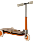 The Maileg Kick Board by Maileg is a vintage-style children's scooter featuring wooden details, an orange frame, white handlebars, and three white wheels, displayed against a plain background.