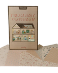 A Maileg Furniture play set box from Maileg stands upright, featuring illustrated rooms on the front. Surrounding it are patterned wallpaper sticker sheets and a variety of colorful Maileg dollhouse furniture pieces.