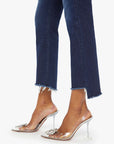 A person wears Mother’s The Insider Crop Step Fray high-waisted bootcut dark blue jeans and clear pointed-toe heels with front embellishments, set against a white background.