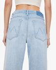 Back view of a person wearing Mother’s The Dodger Button Hover Cuff high-waisted, light blue denim slouchy jeans with back pockets, visible stitching, a blue patch near the waistband, and a white cropped knit top.