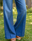 A person wearing the NYC Trouser by Frank & Eileen and tan open-toe sandals stands on grass with blurred greenery in the background.