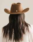 A person with long brown hair and a light shirt is seen from behind wearing the Faire Charlie Western Hat, set against a neutral background.