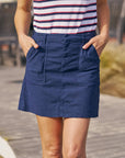 Someone stands outdoors on a wooden walkway wearing the Frank & Eileen Jameson Skirt with contour waistband and utility pockets, paired with a white top featuring red and navy blue horizontal stripes.
