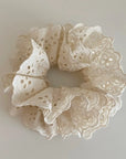 Faire Hair Scrunchies: Cream-colored lace with delicate floral cut-outs, styled in a circular shape on a plain light background—a charming pick for lovers of elegant hair accessories.