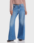 Wearing The Lemon Twist Sneak by Mother—high-rise, wide-leg blue jeans in a five-pocket style—a person stands against a plain white background, with only their lower half and a brown and white striped top visible.