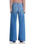 A person is shown from the back wearing Mother’s The Lemon Twist Sneak jeans in light blue with a high-rise, five-pocket style, stitched back pockets, frayed hems, and a red and white striped long-sleeve top.