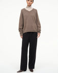 Brown V-neck sweater layered over beige turtleneck, paired with black pants and Staud Wally Sock Flat boots.