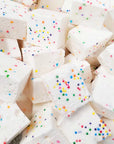 A stack of Faire Funfetti Marshmallows—white, allergy-friendly cubes topped with colorful round sprinkles—are closely arranged together.