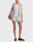 A person in a white t-shirt, Rag & Bone vintage terry mix media sweatshorts, a matching gray sweatshirt over their shoulders, carries a small beige handbag and wears brown sneakers.