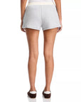 A person is shown from the back, wearing Rag & Bone vintage terry mix media sweatshorts in light gray with a white waistband and hip pockets, paired with dark slip-on shoes. Only their lower back and legs appear against a white background.