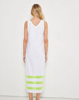 A woman with loose blonde waves faces a white wall, wearing Lisa Todd's "Best Dressed" sleeveless v-neck maxi dress with light green stripes near the hem, paired with matching green sandals.