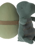 A green fabric toy dinosaur stands by a large, green egg-shaped container with a textured brown band—an ideal accessory for your Maileg Mouse or Maileg mice family collections.