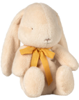 The Maileg Bunny Plush by Maileg is a cream-colored, soft plush bunny with floppy ears, simple stitched face, and a yellow ribbon bow around its neck, sitting upright against a plain white background.