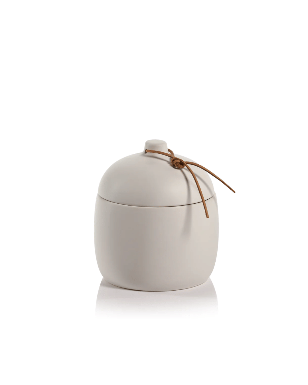 A simple white Zodax ceramic canister with a rounded lid, accented with a thin leather string tied in a bow on a small protruding knob, evokes the rustic aesthetic of a Scottsdale Arizona bungalow. The canister is set against a plain white background.