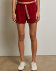 Wearing Perfectwhitetee’s Layla Terry Short in red with an elastic waistband and matching tank top, paired with white sneakers, only the lower half of the person is visible as they stand against a plain wall.