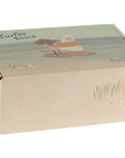 A cardboard box labeled "Maileg Little Sister /Beach Surfer" by Maileg features an illustrated mouse surfing, a grass and sandy beach scene, and suggests a toy mouse in a ruffled one piece with magnetic hands inside.