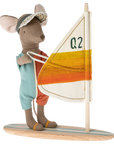 The Maileg Mouse by Maileg wears a visor and aqua-orange outfit, stands on a wooden surfboard, and holds a "Q2"-marked sail with white, yellow, and orange stripes—perfect for fun adventures with your mice family.