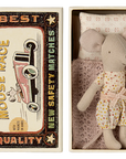 A Maileg Mouse in polka-dot pajamas rests in a small bed with a knitted blanket, tucked inside a matchbox-style box. The Maileg-branded box lid displays vintage text and an image of a mouse driving a red car.