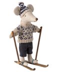 The Maileg Mouse by Maileg wears a knitted sweater, patterned hat, and checkered pants, standing on wooden skis with ski poles—a delightful addition to any mouse collection.