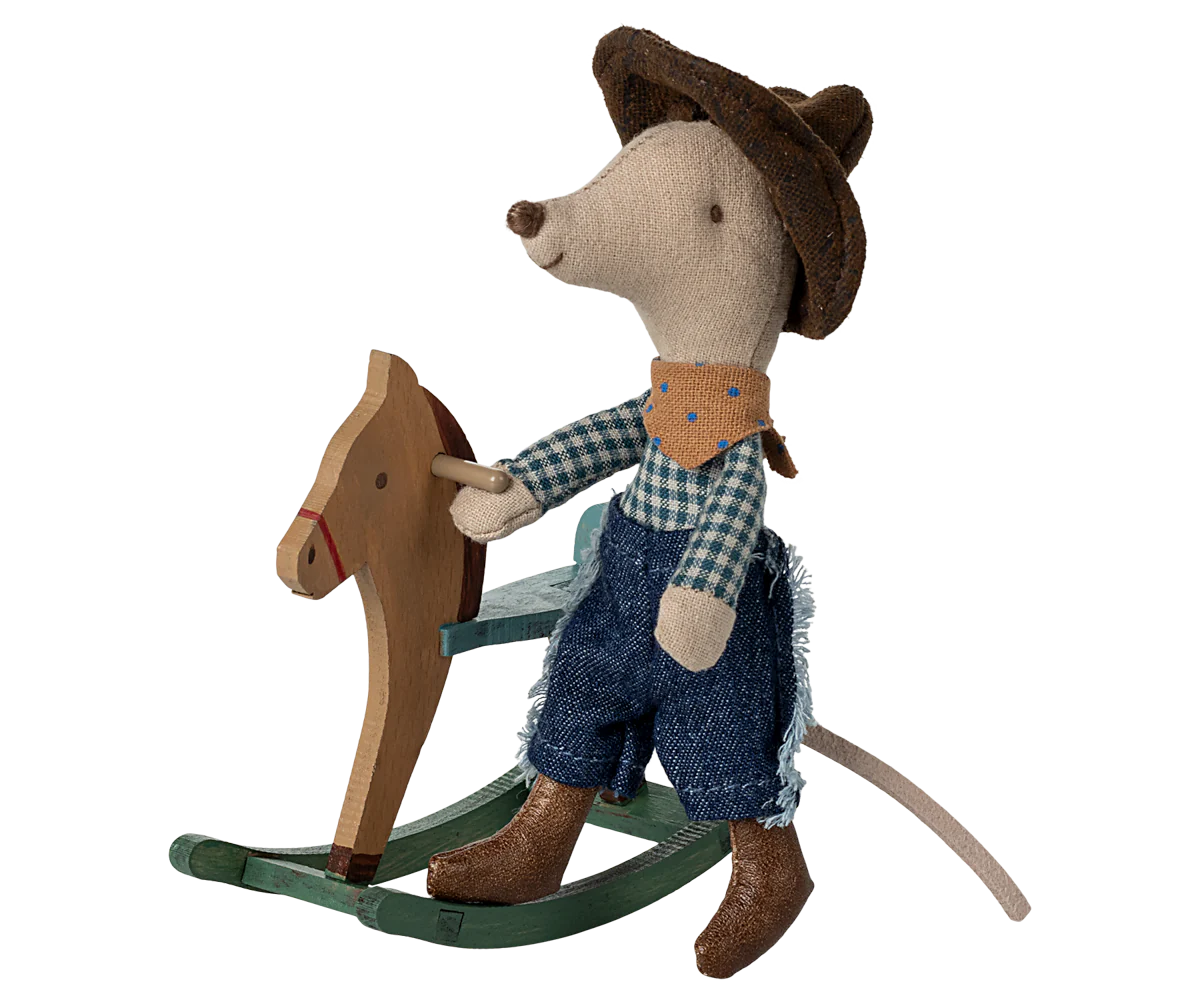 The Maileg Mouse by Maileg is dressed as a cowboy with a hat, scarf, plaid shirt, jeans, and boots, sitting on a wooden rocking horse—a charming addition to any mice family collection.