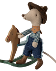 The Maileg Mouse by Maileg is dressed as a cowboy with a hat, scarf, plaid shirt, jeans, and boots, sitting on a wooden rocking horse—a charming addition to any mice family collection.