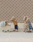 Maileg Mum Mouse, dressed in charming Maileg clothes, pushes a baby mouse in a cream pram while another mouse steers a scooter with two mice. They play on a light rug before a floral-patterned wall.