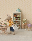 Two Maileg toy mice, including the Maileg Dad Mouse by Maileg, are in a miniature kitchen: Dad sits at a small table with pastries while the other holds a paper bag. Behind them is a shelf with desserts, kitchen items, and cute mouse accessories.