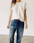 A person wearing Hey Gang’s The Crew 100% cotton plain white short-sleeve tee and blue jeans stands against a plain white wall, with their head partially out of frame.